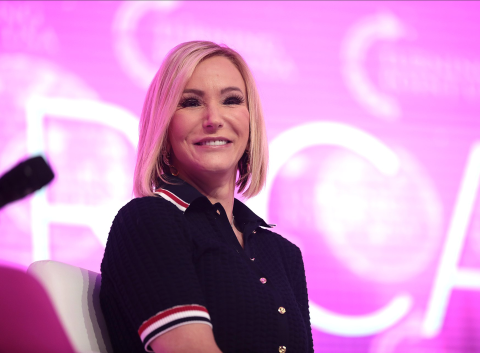 A middle-aged blonde woman in heavy makeup squints at the foreground -- presumably at an audience. 